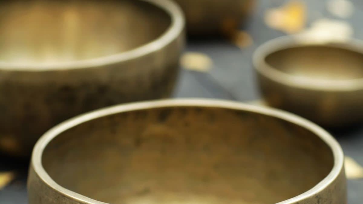 Bols chantants en laiton posés sur un plan de bois, dans une lumière chaude